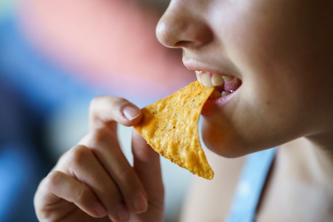Side view of happy teenage girl biting spicy nacho chip at home