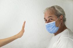 Side view of middle aged man with facemask being stopped by a hand