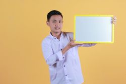 Portrait of a young man in yellow backdrop holding a blank note board