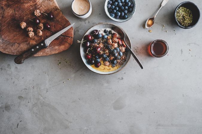 Oat granola yogurt bowl with cherries, blueberries, honey, nuts, coffee, wooden board