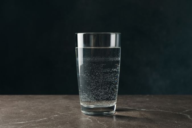 Single glass of water in dark room on marble table