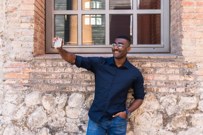 Smiling Black man taking selfie on smartphone near building