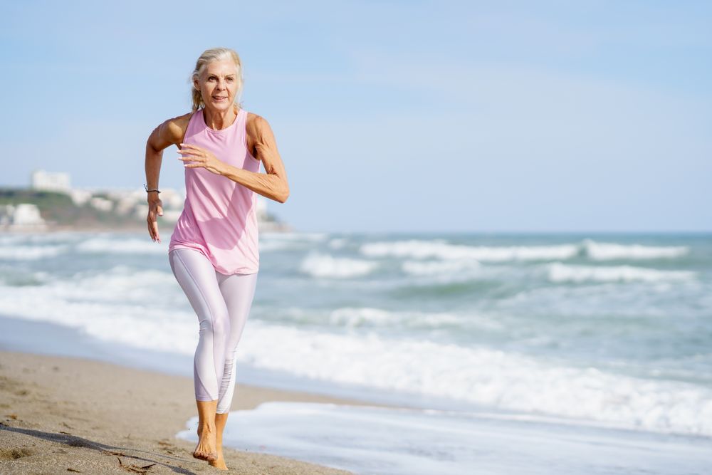 Older female in sports wear jogging along beach