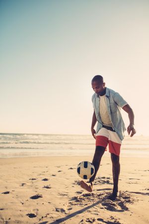 Young man kicking soccer football at the seaside