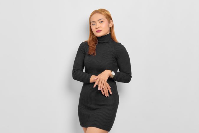 Sultry Asian woman with red hair in dark dress in studio shoot with her hands on her front