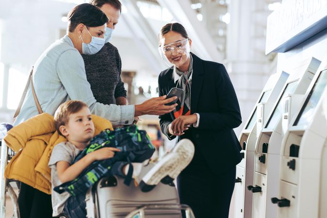 Ground attendant assisting traveler family at self service check-in at airport in pandemic