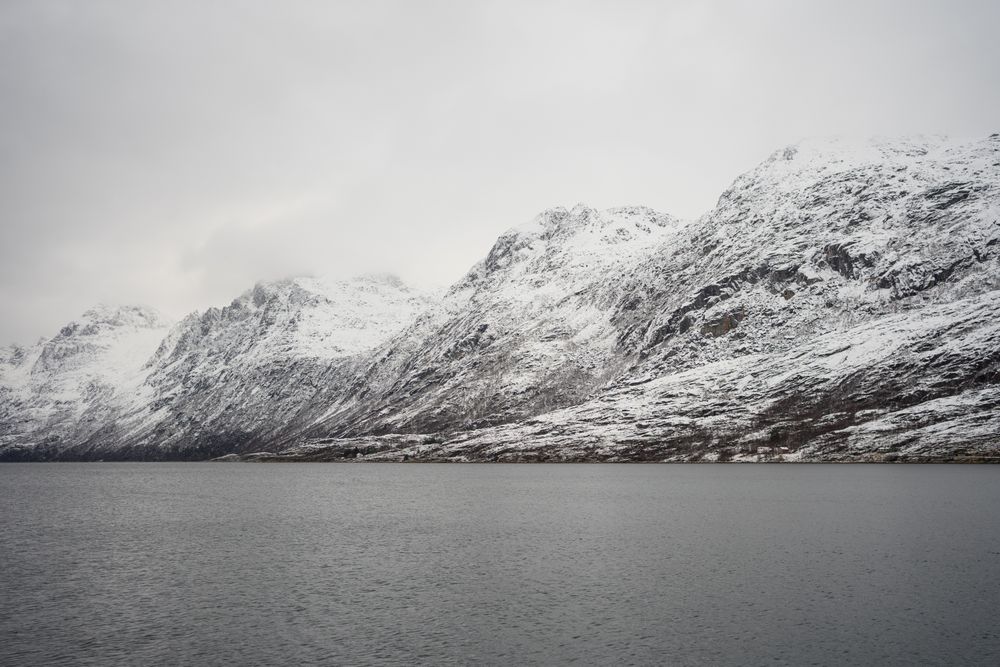 Tranquil lake against snowy hills in cold overcast weather