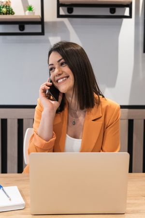 Smiling female freelancer sitting at table with laptop and using a phone