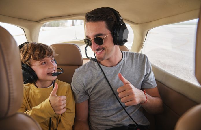 Cheerful young man and child showing thumbs up before flight on