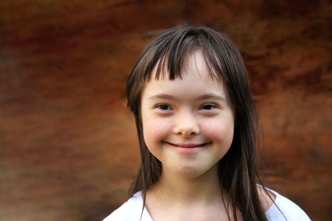 Happy little girl with Down syndrome, brown hair and bangs on brown background