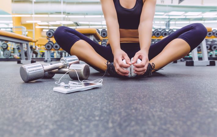 Woman stretching legs on gym floor next to silver weights
