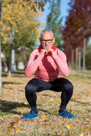 Grey haired man with glasses doing squats in the park