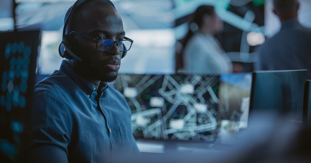 Black Technical Support Manager Using Headphones with Built-In Mic for Communication with Client