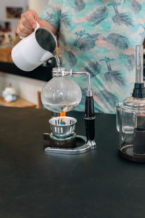 Unrecognizable barista skillfully preparing specialty coffee using Japanese siphon