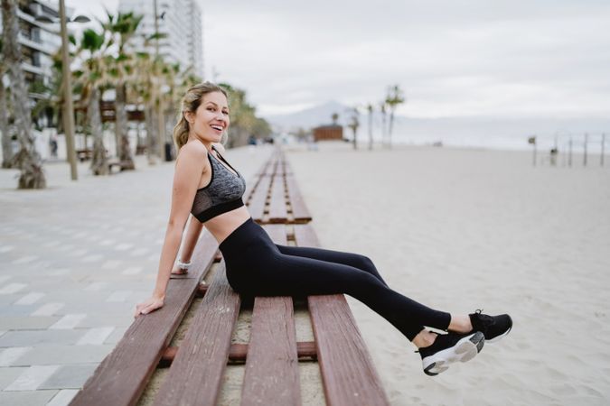 Sportswoman resting in a bench at sandy beach