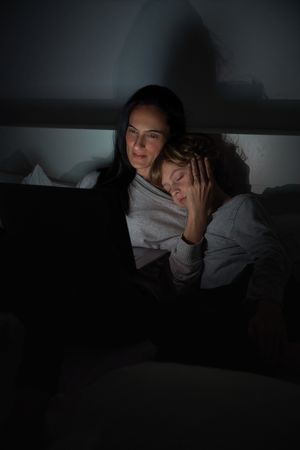 Mother helping sleepy son to do homework in darkness