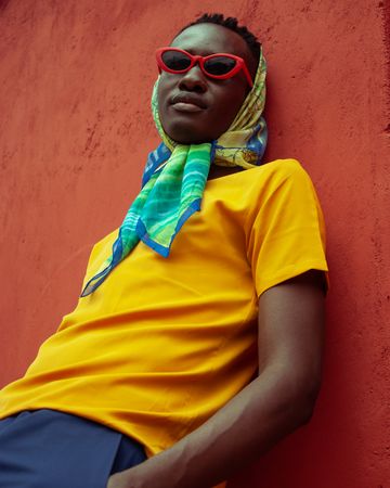 Man wearing headscarf and red framed sunglasses leaning on wall