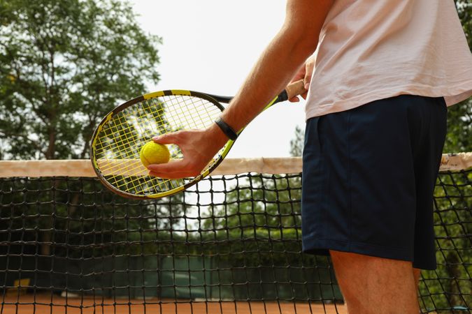 Man hold racket and ball against tennis net