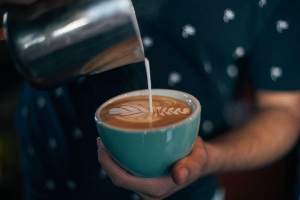 Hand pouring milk into coffee cup