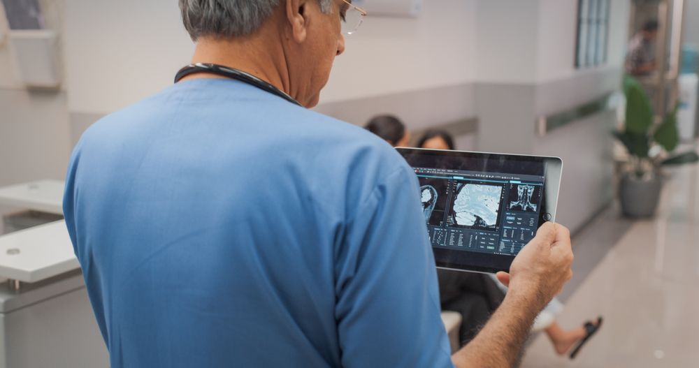 Backview Shot of Indian Doctor Walking in Hospital Corridor, Using a Digital Tablet.