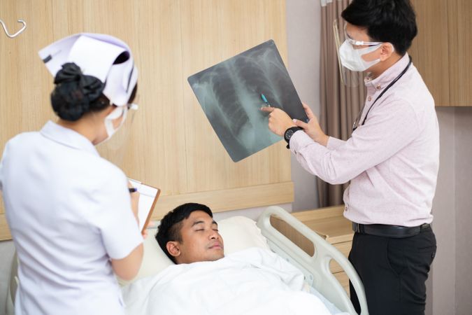 Patient lying in hospital bed with doctor showing chest X-ray