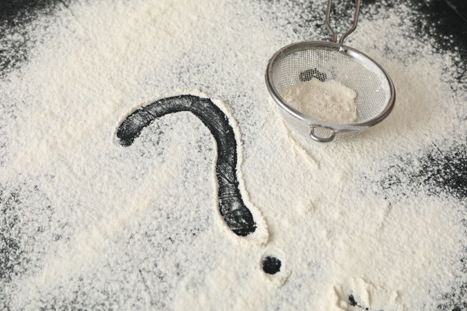 Flour, sieve and question mark on dark background