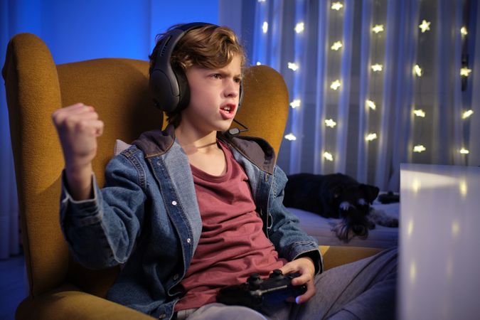 Emotional boy playing video game in room with dog and garland