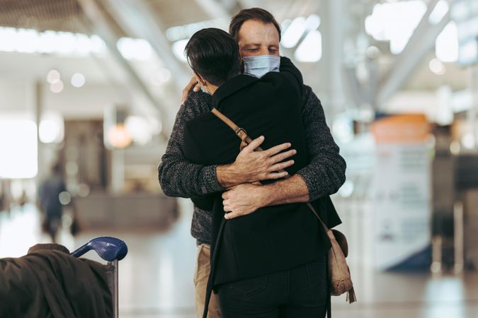 Man giving hug to woman after arrival from trip post pandemic at airport