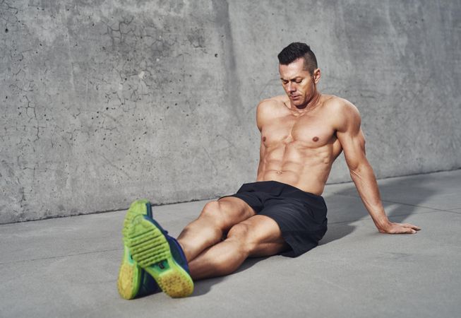 Muscular shirtless man sitting with legs outstretched