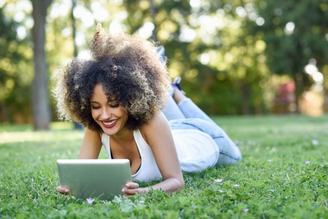 Happy Black woman with afro hairstyle using digital tablet in park