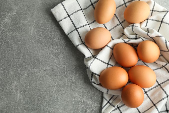 Chicken eggs in kitchen towel on gray background, space for text