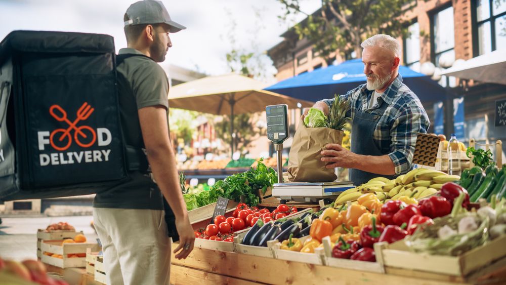 Cheerful Street Vendor Handing Over a Recycled Paper Bag with Fresh Produce