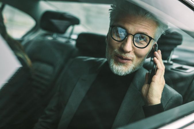 Happy businessman sitting on back seat of a car and talking on the mobile phone