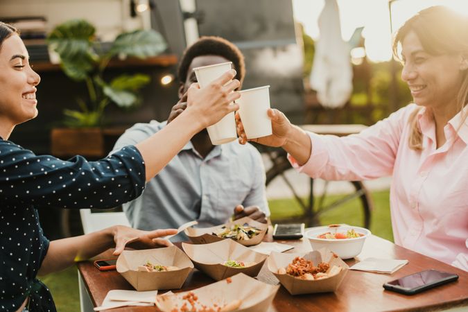 Happy people eating and cheering at food truck restaurant - Focus on girl hand holding cup of drink