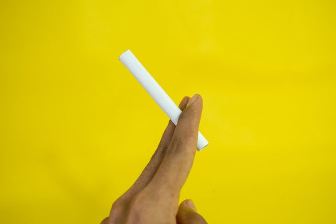 Side view of hand holding cigarette against yellow wall