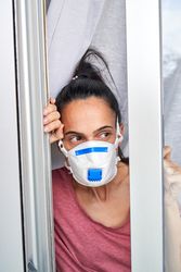 Woman in protective mask looking out window