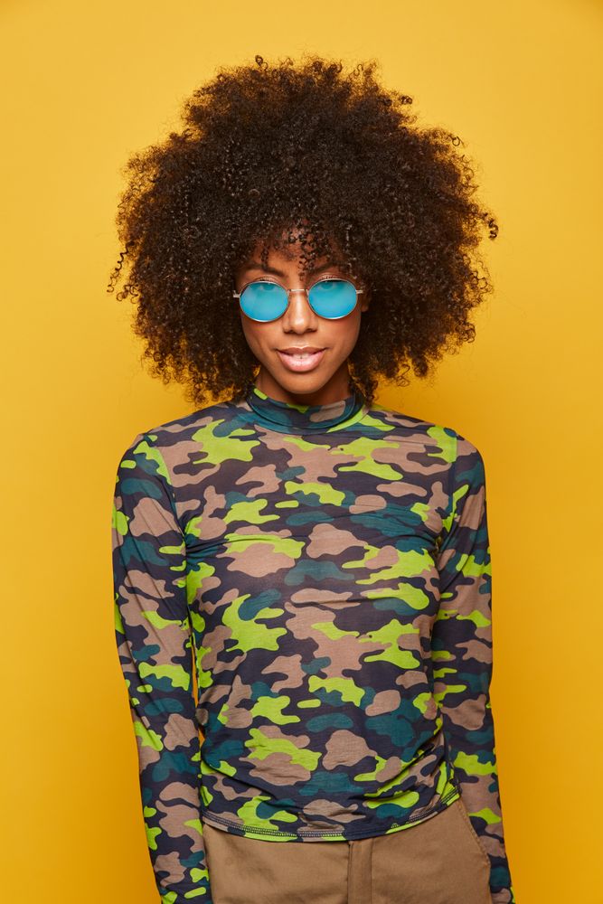 Trendy Black female in sunglasses on bright backdrop
