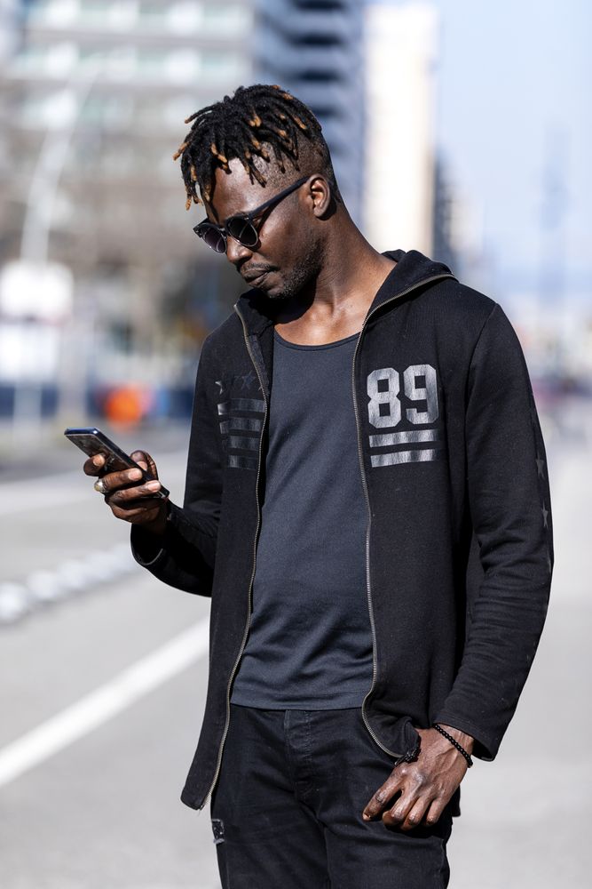 Black smiling man with sunglasses using mobile phone outdoors