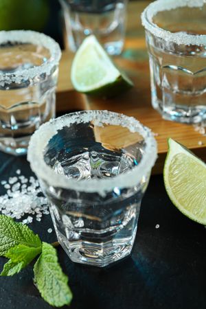 Tequila shots with salt, lime slices and mint on dark table