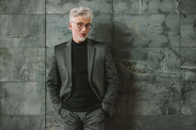 Portrait of handsome mature man in business suit standing on grey wall