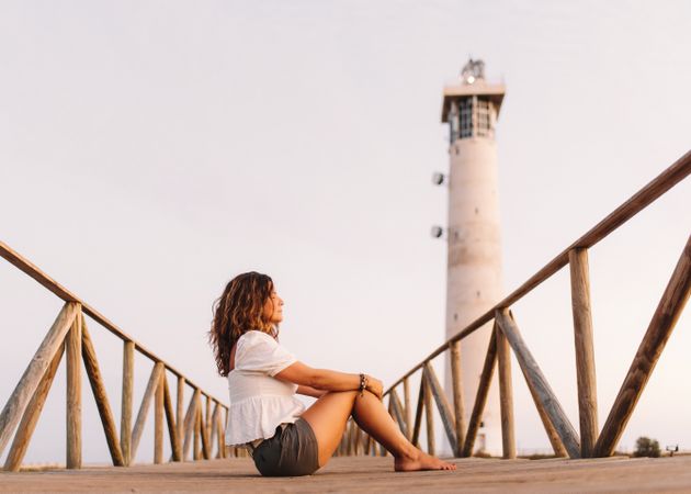 Woman sitting on bridge to lighthouse and looking away