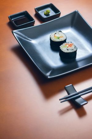 Two freshly made sushi rolls on rectangular plate on table, ready to eat