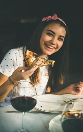 Young woman smiling eating pizza outside in the sun, with red wine