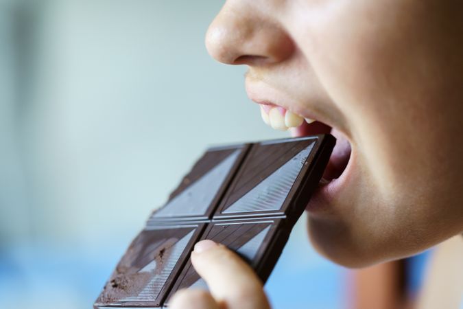 Side view of girl biting into square of dark chocolate