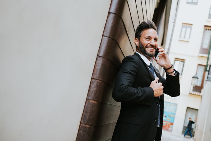 Adult stylish man in costume talking on smartphone near wall