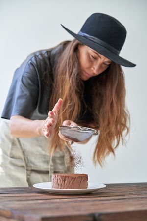 Female sifting chocolate powder through sieve on cake