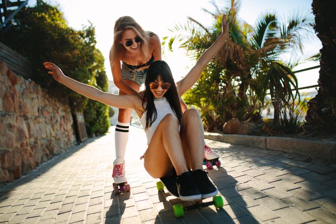 Two female friends playing with skateboard on a summer day