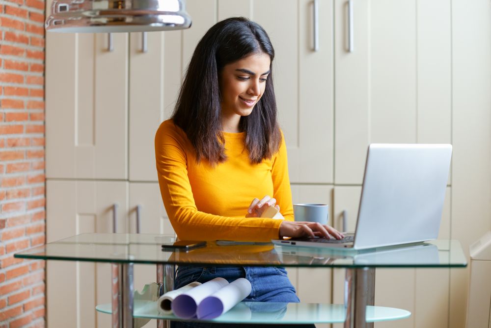 Persian female working at home with a laptop and blueprints underneath her desk