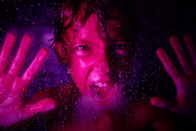 Crop angry boy screaming behind wet glass wall