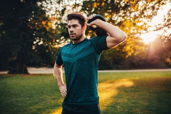 Portrait of tough young guy exercising with kettlebell in park